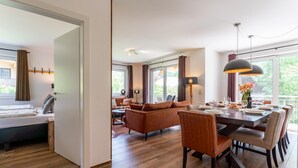 A modern hotel room with a dining area, wooden flooring, and large windows.