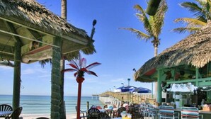 A beachside restaurant with outdoor seating, palm trees, and a view of the ocean. - PLACE TO BE we have everything you need  (North Port)