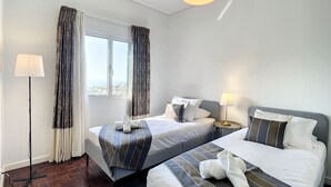 A hotel room with two beds, a window with curtains, a standing lamp, and a view of the city. - Santa Rita House by Atlantic Holiday (Funchal)
