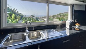 A kitchen with a stainless steel sink, a window with a view of a cityscape and greenery, and a small plant on the counter. - Santa Rita House by Atlantic Holiday (Funchal)