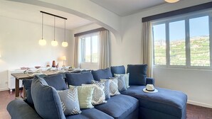 A modern living room with a sectional sofa, dining table, and large windows offering a view of the countryside. - Santa Rita House by Atlantic Holiday (Funchal)