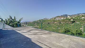 Une terrasse dallée, agrémentée d’une clôture en métal, qui offre une vue sur une colline parsemée de bâtiments et de verdure.