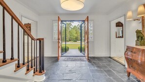 A hallway with a stone floor, wooden staircase, and a view through glass doors to a garden. - TheGrey -Spacious,Eclectic,Home in a Serene Setting (Statesboro)