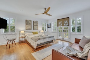 A spacious bedroom with a large bed, a ceiling fan, and a view through a sliding door to the outdoors. - TheGrey -Spacious,Eclectic,Home in a Serene Setting (Statesboro)