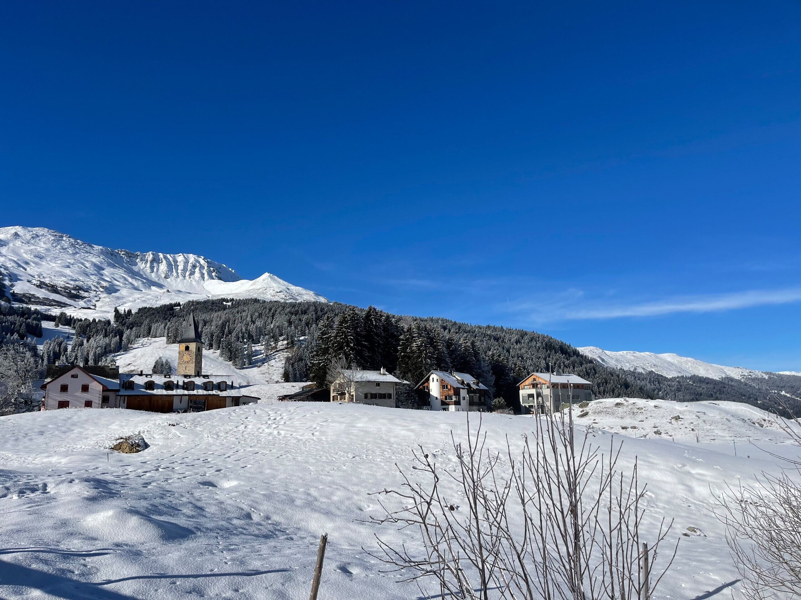 Un pueblo cubierto de nieve con una iglesia y edificios residenciales, rodeado de montañas.
