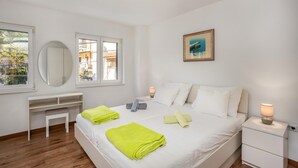 A bedroom with a bed, bedside tables, a desk, a chair, and a window with a view of buildings.