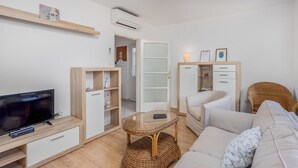 A modern living room with a flat-screen TV, a wicker coffee table, a sofa, and a built-in wardrobe with drawers.