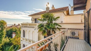 A building with a balcony, a palm tree, and a view of the sea.