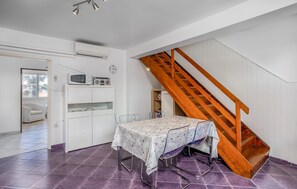 A room with a wooden staircase, a white cabinet with a microwave and radio, a dining table with a floral tablecloth, and purple-tiled flooring. - Amazing home in Opatija with WiFi (Opatija)