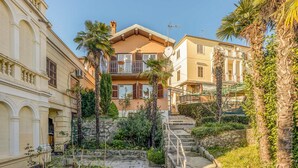 A multi-story building with balconies, a stone staircase, and surrounding greenery.