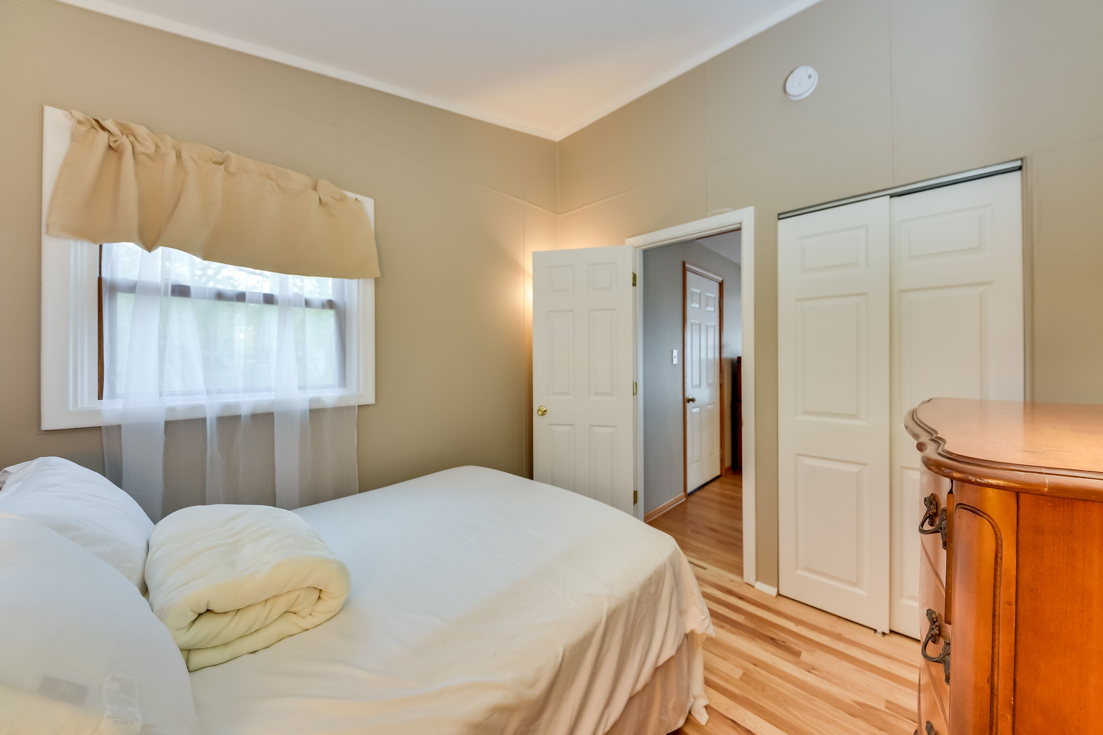 A bedroom with a bed, a wooden dresser, and two white doors leading to other rooms.