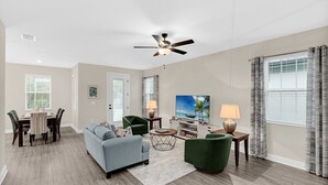 Un salon spacieux doté d’un ventilateur de plafond, d’un téléviseur et d’un coin repas avec des chaises et une table.