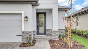 Une maison moderne avec un garage, une porte d’entrée dotée d’un panneau de verre et un petit arbre dans le jardin.