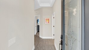 Un couloir avec un luminaire au plafond, une porte vitrée et un tableau encadré accroché au mur.