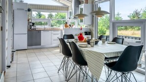 Et moderne køkken med spiseplads, store vinduer og udsigt til grøn natur.