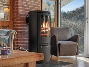 Ein Kaminofen, ein gepolsterter Sessel und ein Holztisch mit Kerzen.