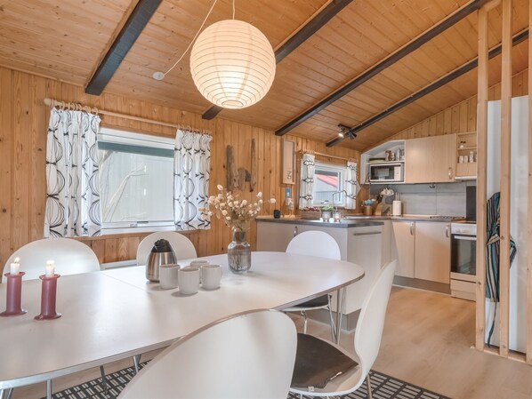 A wooden interior with a dining table, chairs, a kitchen area, and a hanging light fixture.