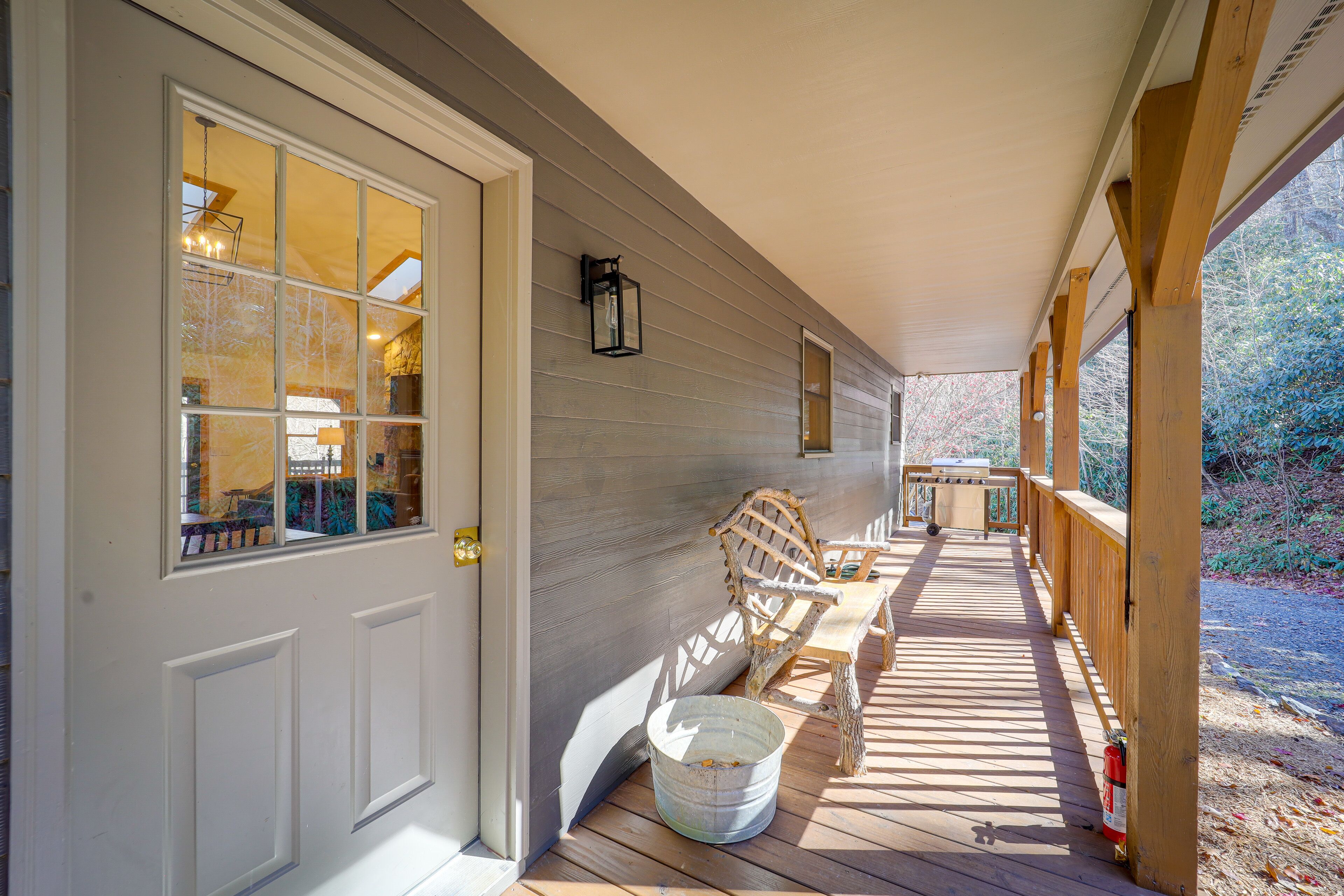 A covered porch with a wooden bench, a metal bucket, and a fire extinguisher.