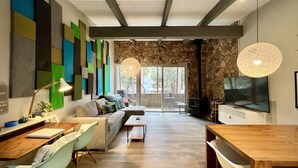 A modern living room with a sofa, coffee table, and dining area. There is a fireplace and a TV mounted on the wall.