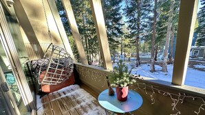 A wooden deck with a small table and a potted plant, overlooking a snowy landscape with trees.