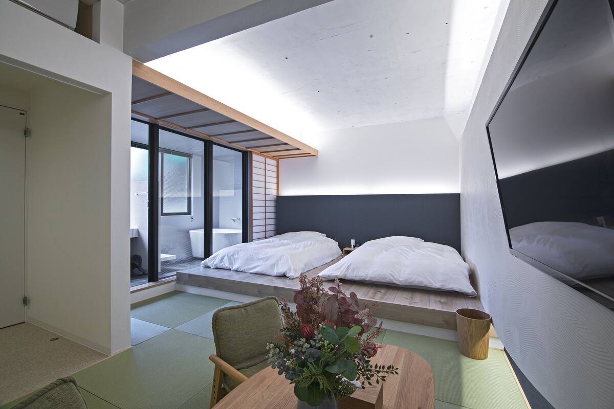 A modern hotel room with a large bed, a small seating area, and a view of the outside.