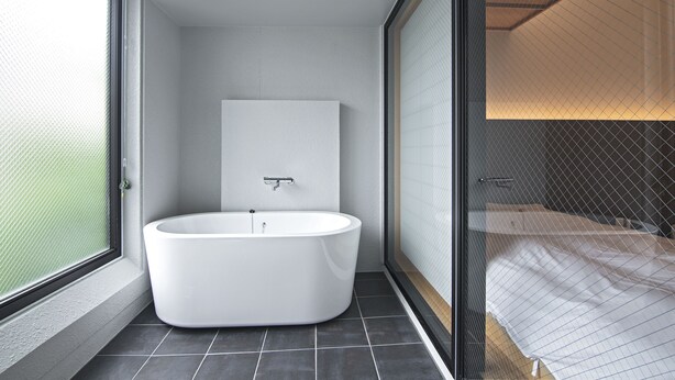 A modern bathroom with a freestanding bathtub, a large mirror, and a glass partition separating the bathroom from the bedroom. - Forest Guardian Hotel 京都御所西 (Kyoto)