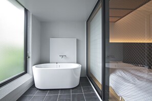 A modern bathroom with a freestanding bathtub, a large mirror, and a glass partition separating the bathroom from the bedroom. - Forest Guardian Hotel 京都御所西 (Kyoto)