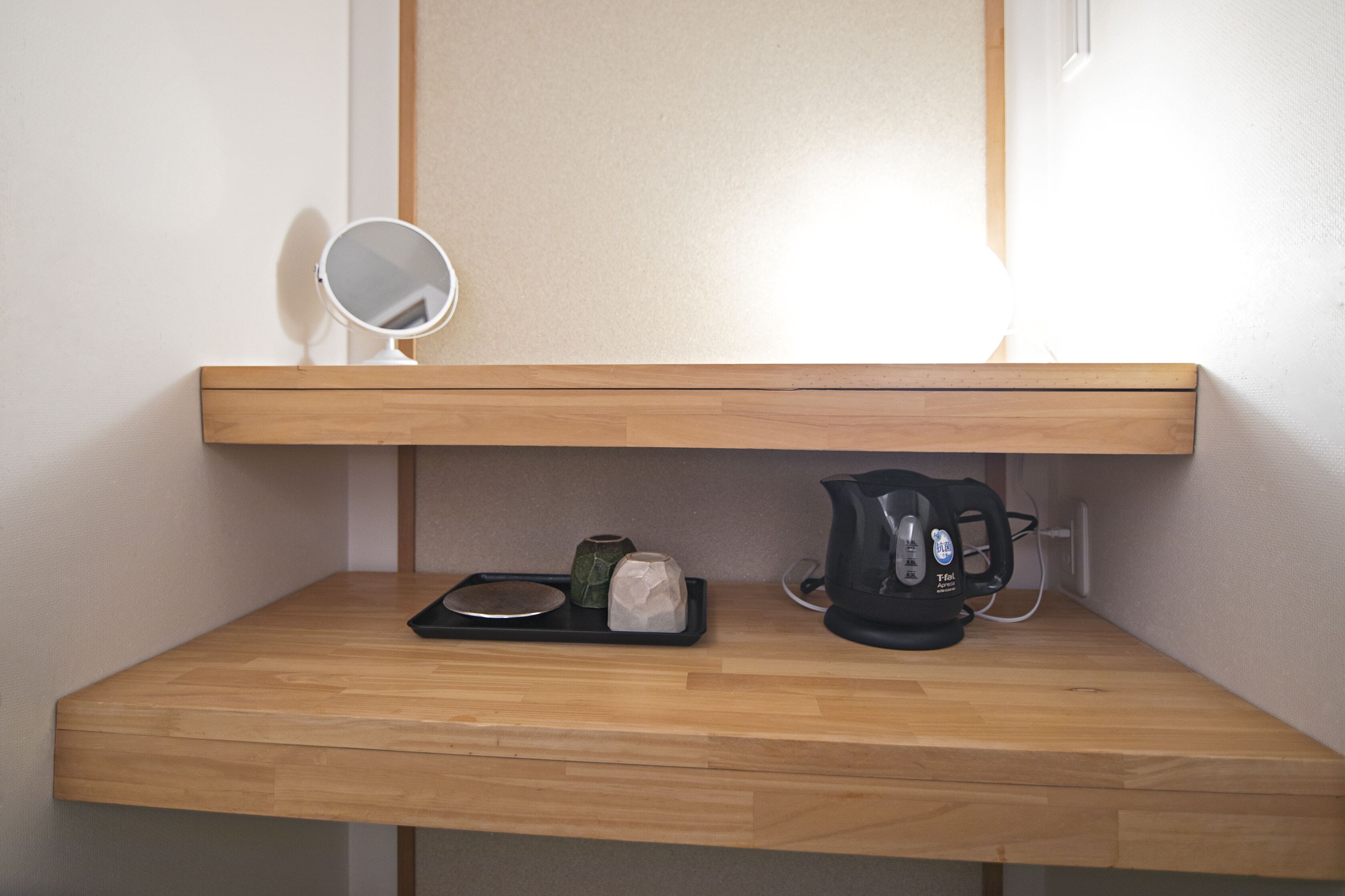 Un petit bureau en bois, avec une bouilloire, un plateau et un miroir.