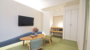 A room with a flat-screen TV mounted on the wall, a round wooden table with two chairs, a small vase with flowers, and a large mirror above a shelf. - Forest Guardian Hotel 京都御所西 (Kyoto)