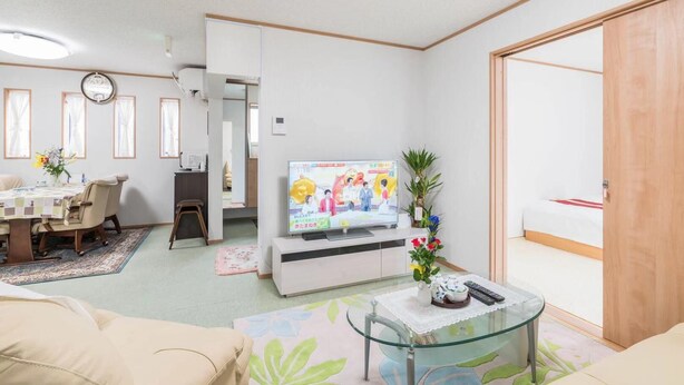 Una sala de estar con televisión, un comedor con mesa y sillas, un sofá y una pequeña mesa de centro.