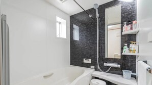 Un baño moderno con una bañera blanca, un taburete pequeño blanco, un tocador con espejo y una ducha con pared de mármol negro.