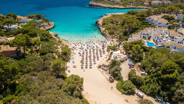 Oversigtsbillede af et kystresort med strand, klart blåt vand og forskellige bygninger.