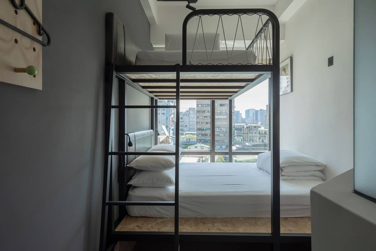 Habitación con literas, vista a la ciudad, piso de madera y estante en la pared.