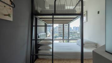 A bunk bed room with a city view, a wooden floor, and a wall-mounted shelf.