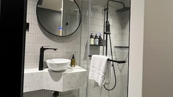A modern bathroom with a round mirror, a white sink, a glass shower enclosure, and a white toilet.
