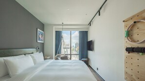 Une chambre d’hôtel avec un grand lit, un téléviseur fixé au mur et une vue sur la ville par la fenêtre.