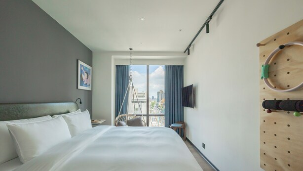 A hotel room with a large bed, a television mounted on the wall, and a view of the city through the window. - Hanns Summer (Taipei)