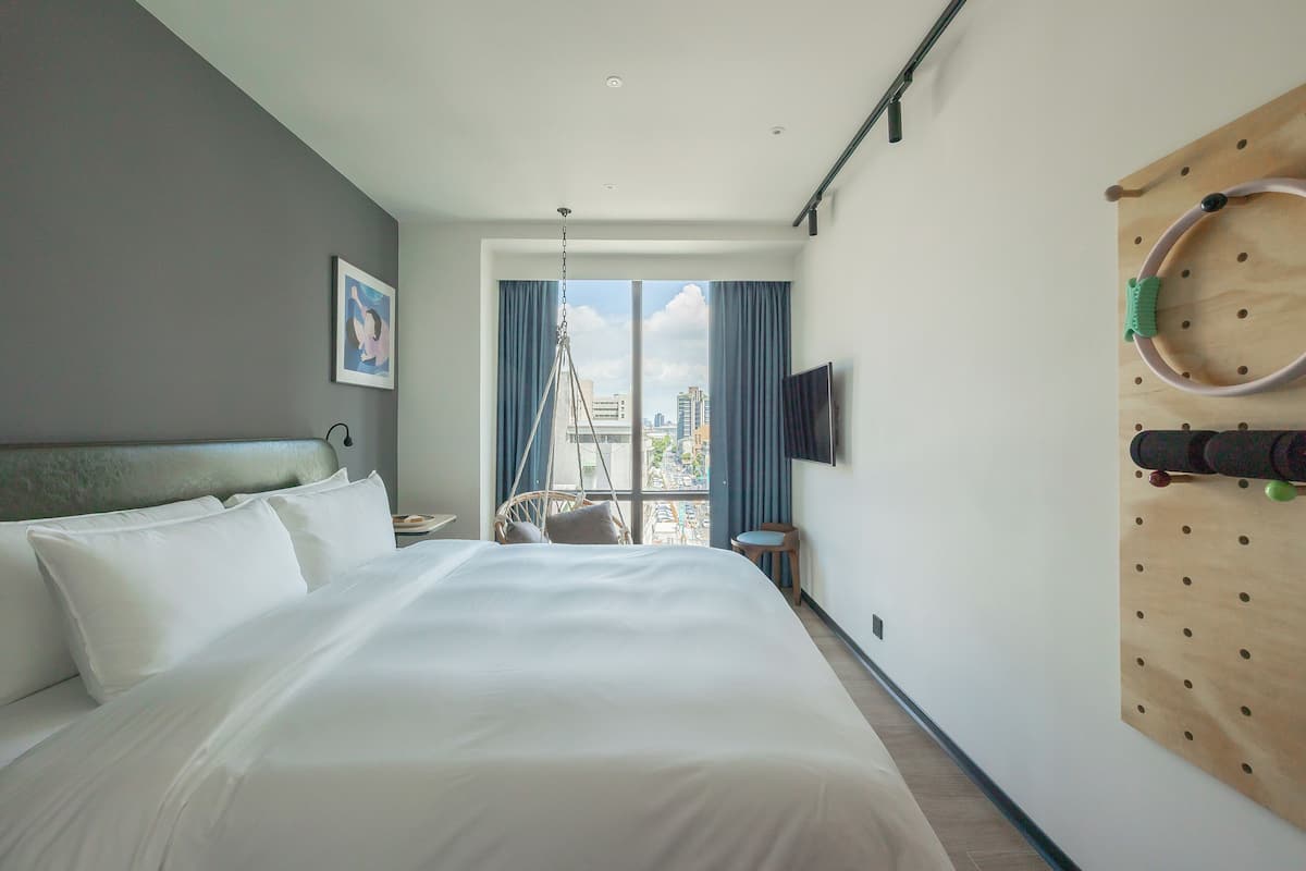 Habitación de hotel con una cama grande, un televisor montado en la pared y vistas de la ciudad a través de la ventana.