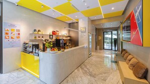 A hotel reception area with a modern design, featuring a bright yellow and white color scheme, a marble floor, and a seating area with cushions. - Hanns Summer (Taipei)