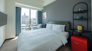A modern hotel room with a large bed, a small table, a red suitcase, and a city view through the window. - Hanns Summer (Taipei)