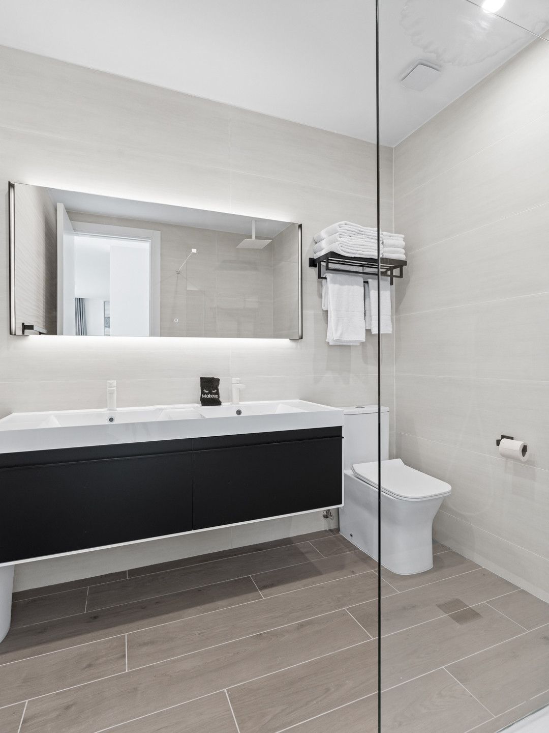 A modern bathroom with a large mirror, a black vanity, a toilet, and a glass shower enclosure.