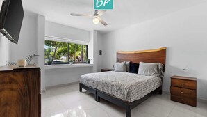Un dormitorio moderno con cama, mesitas de noche, ventilador de techo y ventana con vistas a zonas verdes.