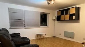 A spacious living room with a wooden floor, a black sofa, a small white table, and a floor lamp. - Charming 2bedroom Retreat in Great Barr/hamsted (Birmingham)