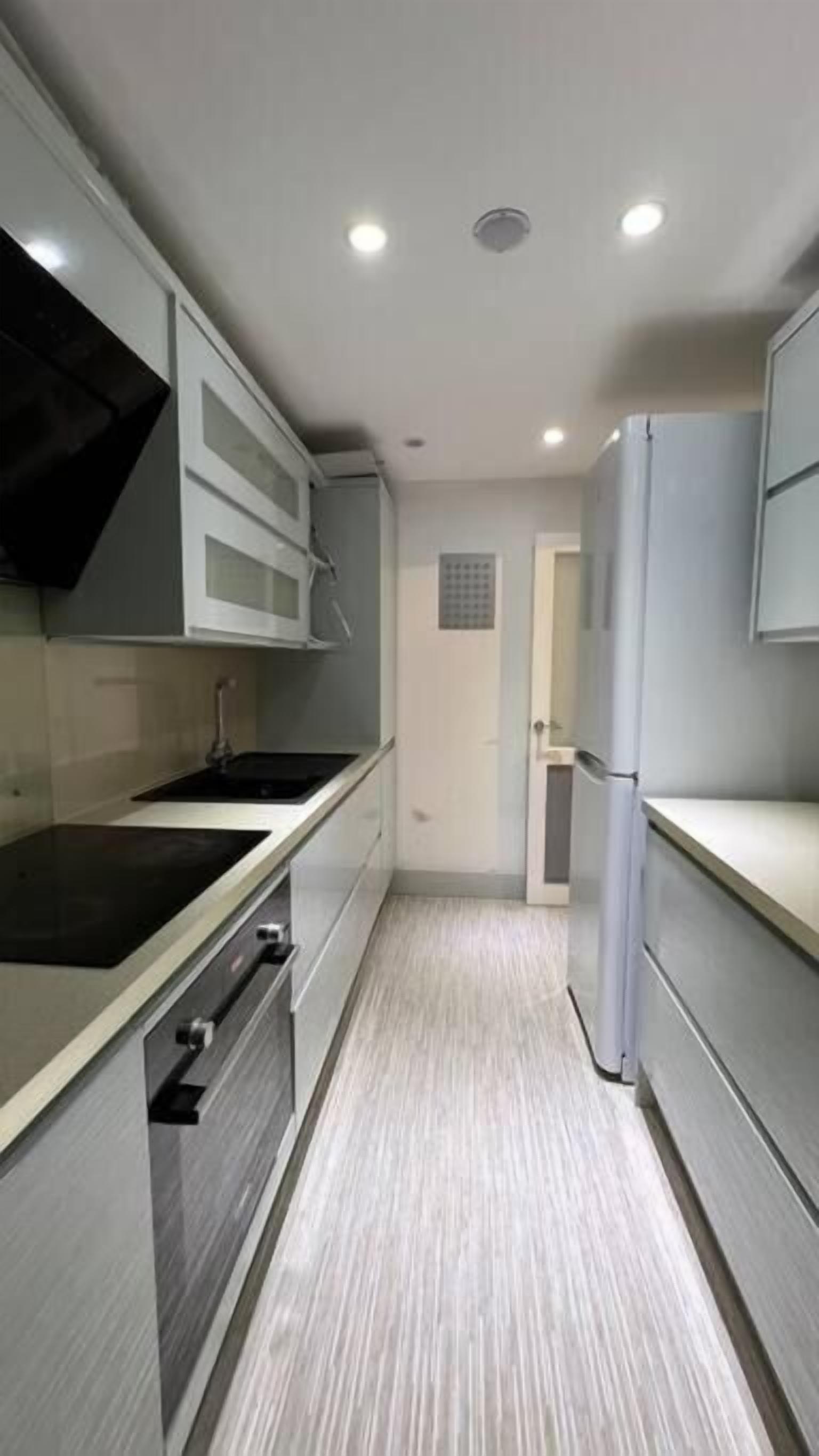 A narrow kitchen with white cabinets, a black stove, and a white refrigerator.