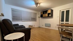 A living room with a black leather sofa, a small white table, a wooden dining table, and a ceiling light fixture. - Charming 2bedroom Retreat in Great Barr/hamsted (Birmingham)