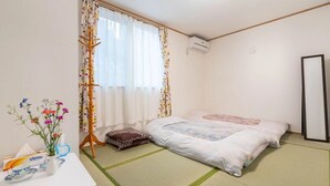 Une pièce comprenant un lit, un futon, un présentoir en bois, un vase avec des fleurs et une table sur laquelle se trouvent une boîte et une tasse.