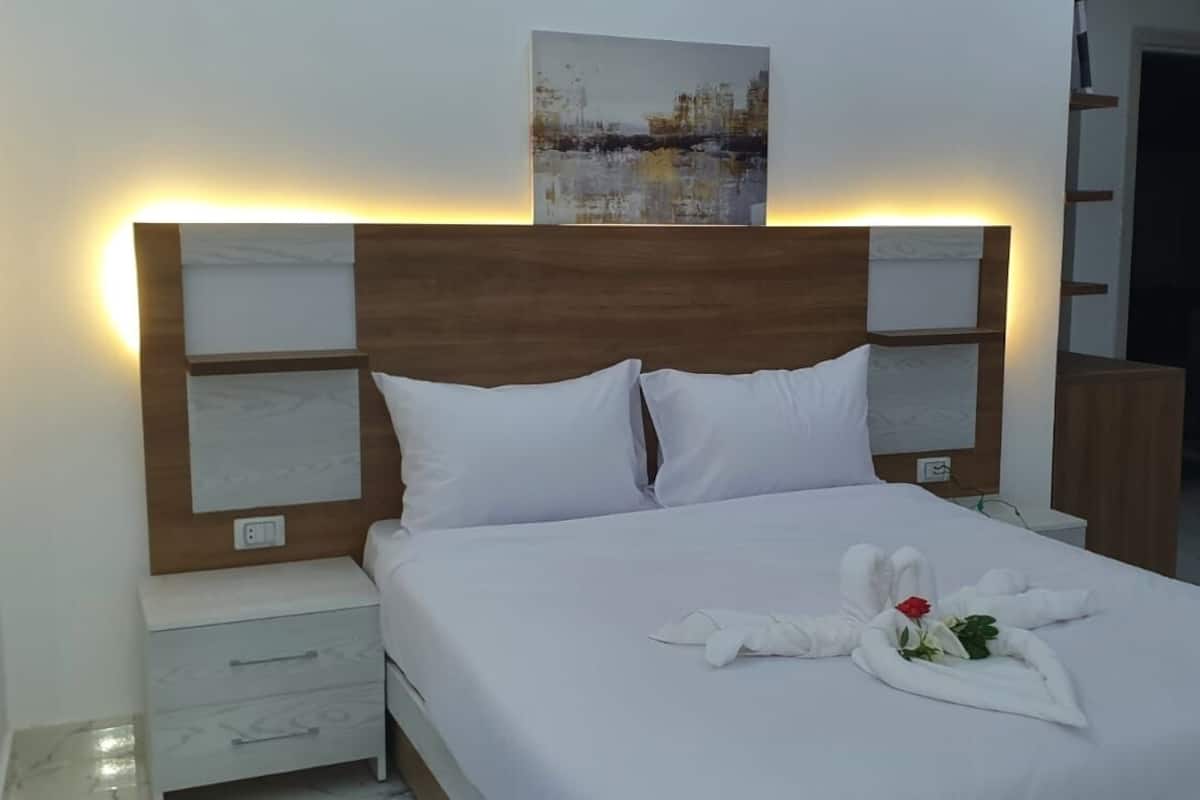A neatly made bed with white linens and a decorative towel arrangement featuring a rose.
