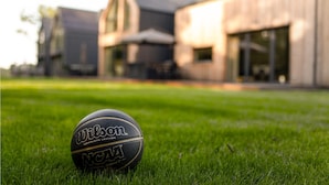A basketball on a grassy lawn with a building in the background.