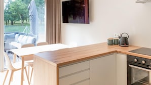 A modern kitchen with a wooden countertop, a kettle, and a stove. There is a dining area with a table and chairs visible through the window.