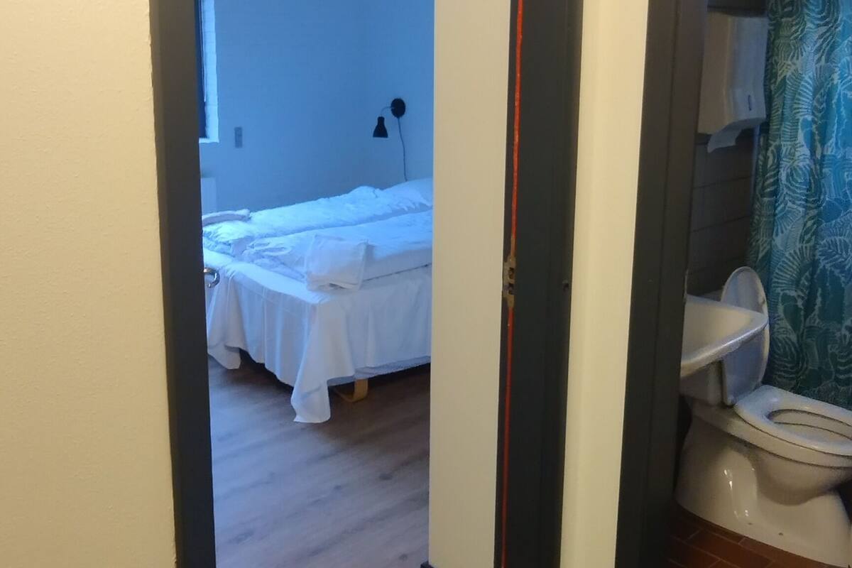 A hallway with a wooden floor leading to a bedroom with a bed and a bathroom with a toilet and a shower curtain.